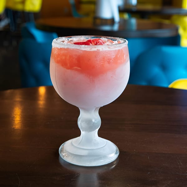 A frosty strawberry margarita with a salted rim and fresh strawberries on a dark wooden table.