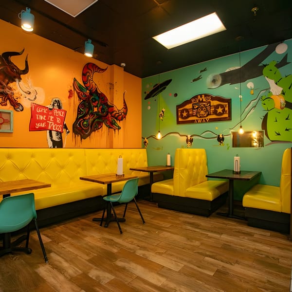 Vibrant Hacienda Tacos interior with yellow booths, teal chairs, and colorful murals on orange and green walls.