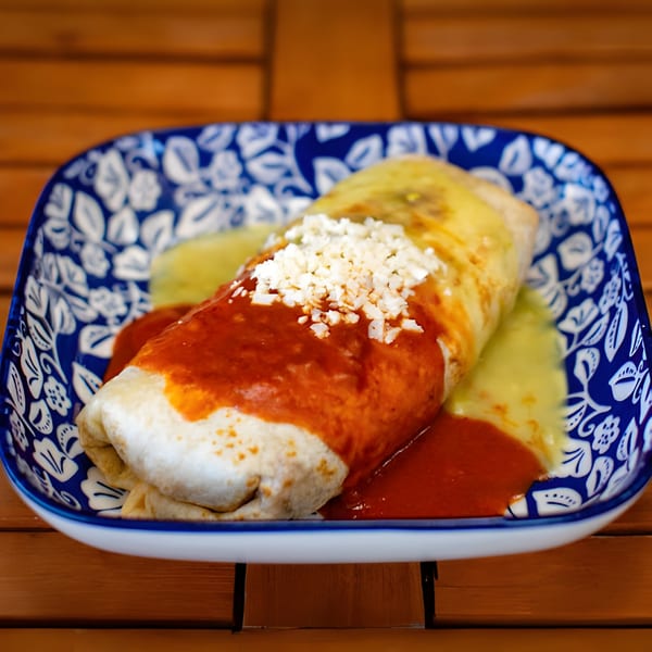 Hacienda Tacos' burrito covered in red and green sauce, topped with crumbled white cheese, on a blue and white plate.