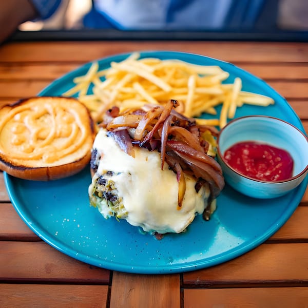 A burger with melted cheese and caramelized onions, fries, and ketchup on a blue plate.