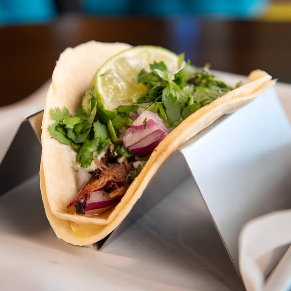 A Hacienda Tacos Mexican taco with meat, red onions, cilantro, and a lime wedge in a metal holder.