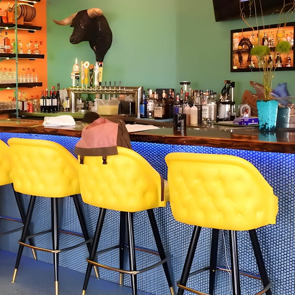 Hacienda Tacos bar with yellow stools, a bull head, and bottles on shelves.