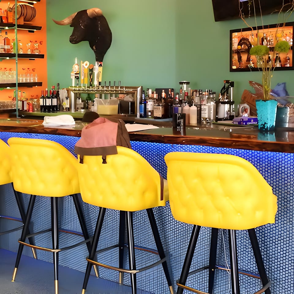 Hacienda Tacos bar with yellow stools, a bull head, and bottles on shelves.