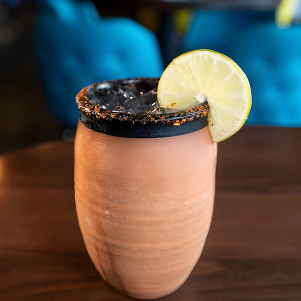 A Hacienda Tacos Mexican drink in a clay cup with a chili-lime rim and a lime wedge.