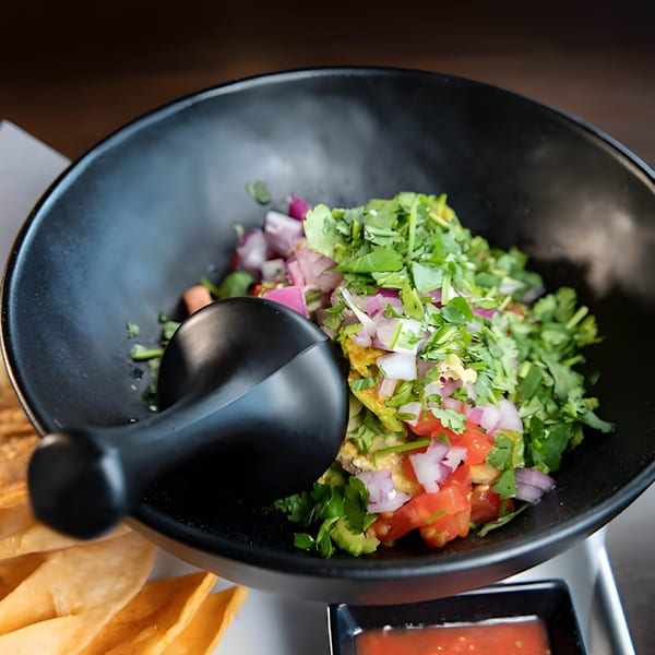 Fresh guacamole with red onions, tomatoes, and cilantro in a black bowl with tortilla chips and salsa.