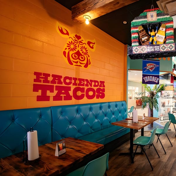Hacienda Tacos interior with orange walls, teal booth seating, wooden tables, and a hanging Modelo beer piñata.