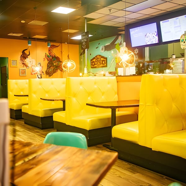 Interior of Hacienda Tacos with bright yellow booths, wooden tables, and colorful murals on the walls.