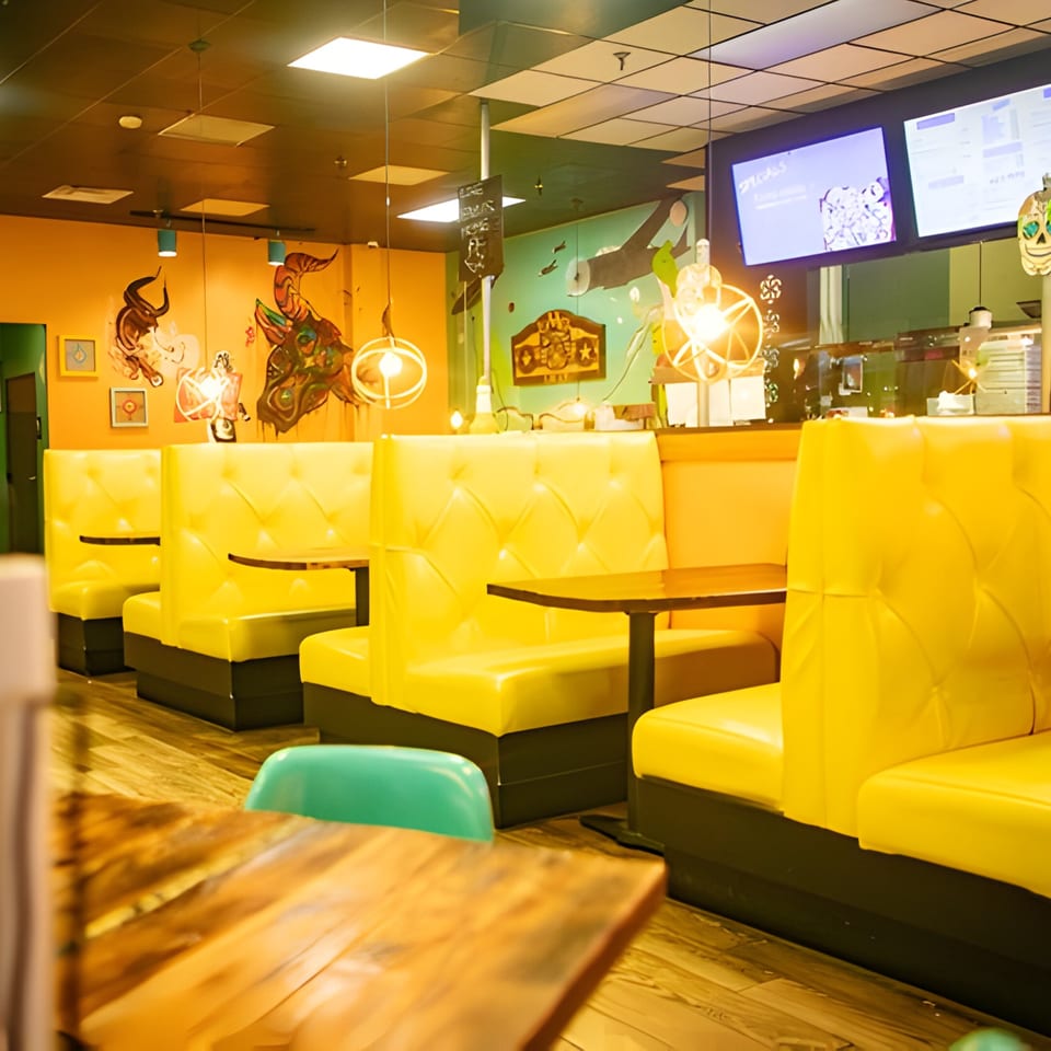 Interior of Hacienda Tacos with bright yellow booths, wooden tables, and colorful murals on the walls.