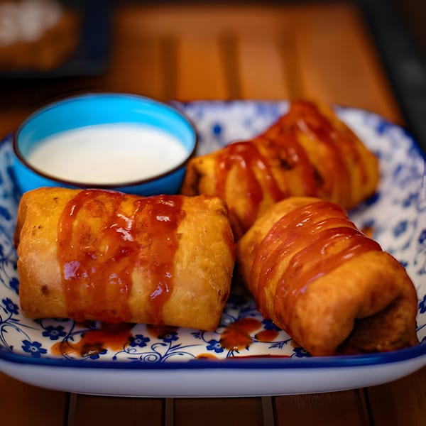 Three Hacienda Tacos Mexican egg rolls drizzled with sauce, served with a side of white dipping sauce.