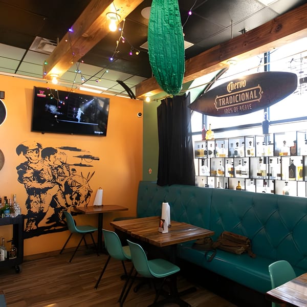 Interior of Hacienda Tacos, featuring orange walls, teal seating, wooden tables, and a Cuervo sign.
